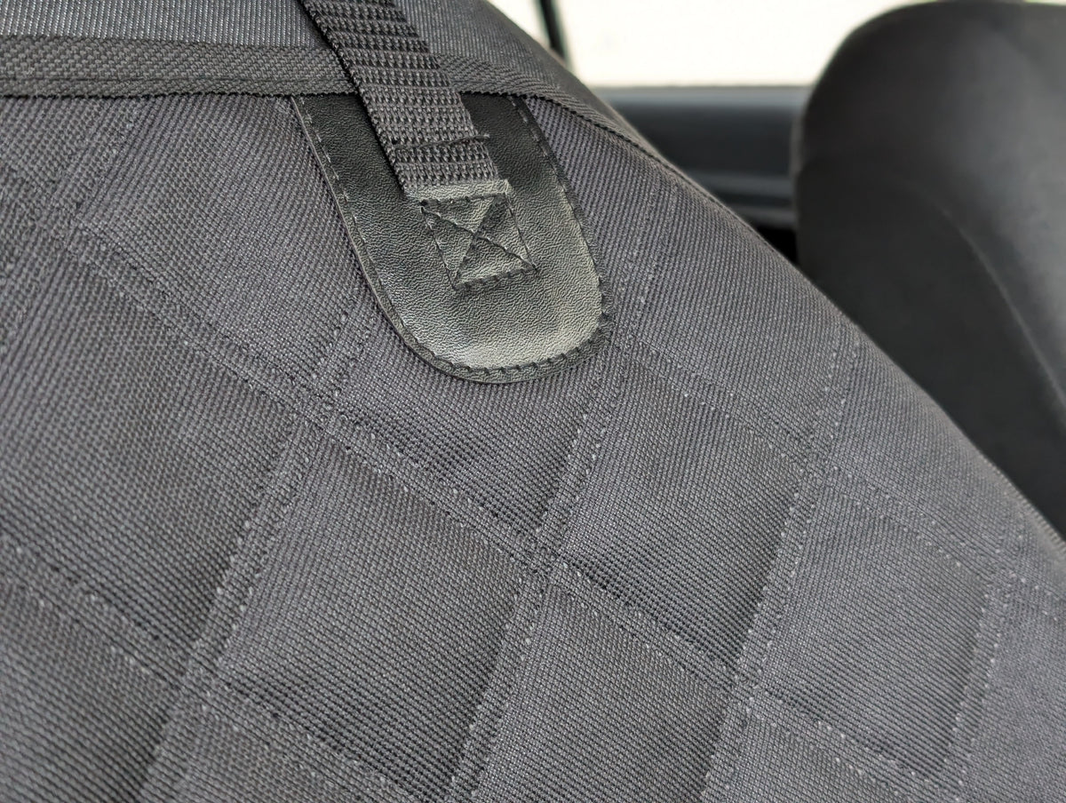 Dark gray seat protector panel with stitched webbing strap and embroidered logo patch
